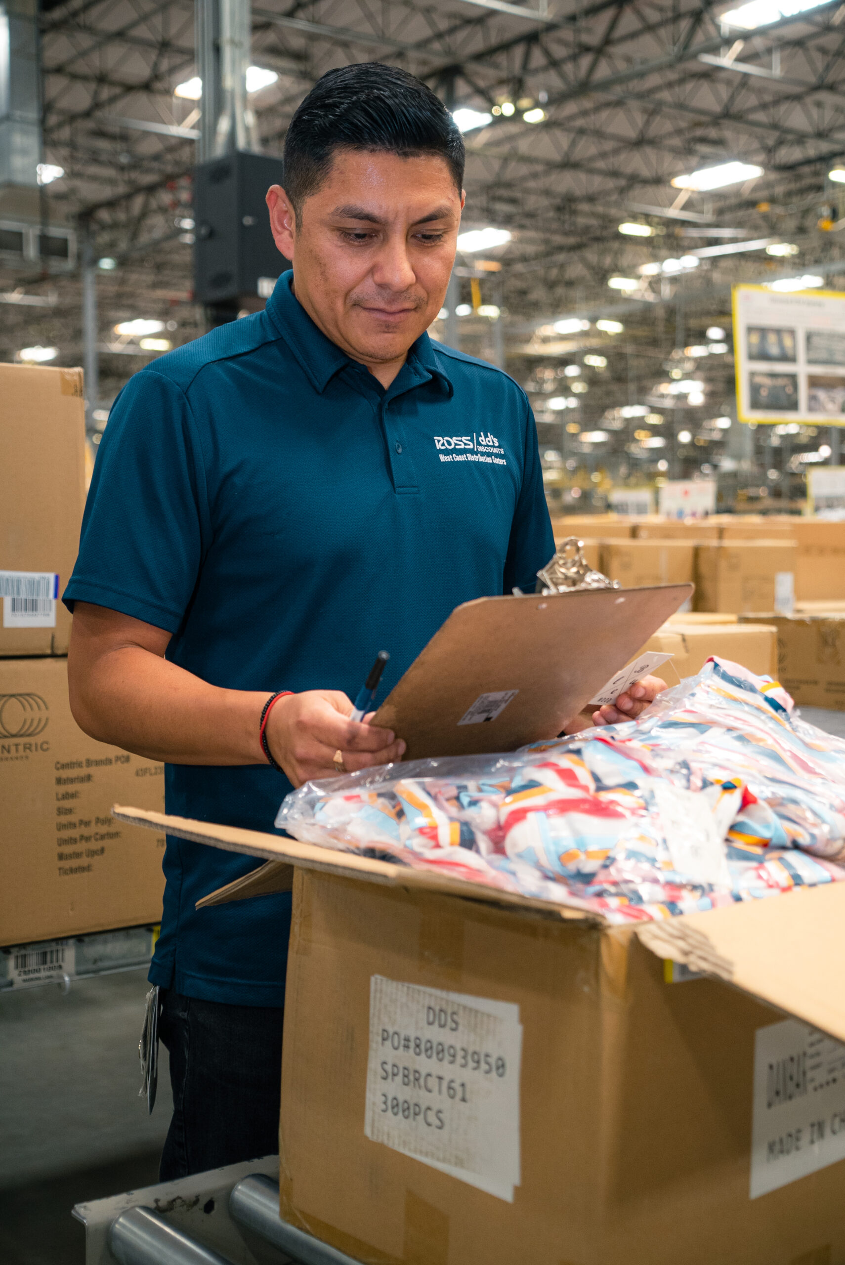 Ross Associate in a warehouse looking at a clipboard and merchandise in a box